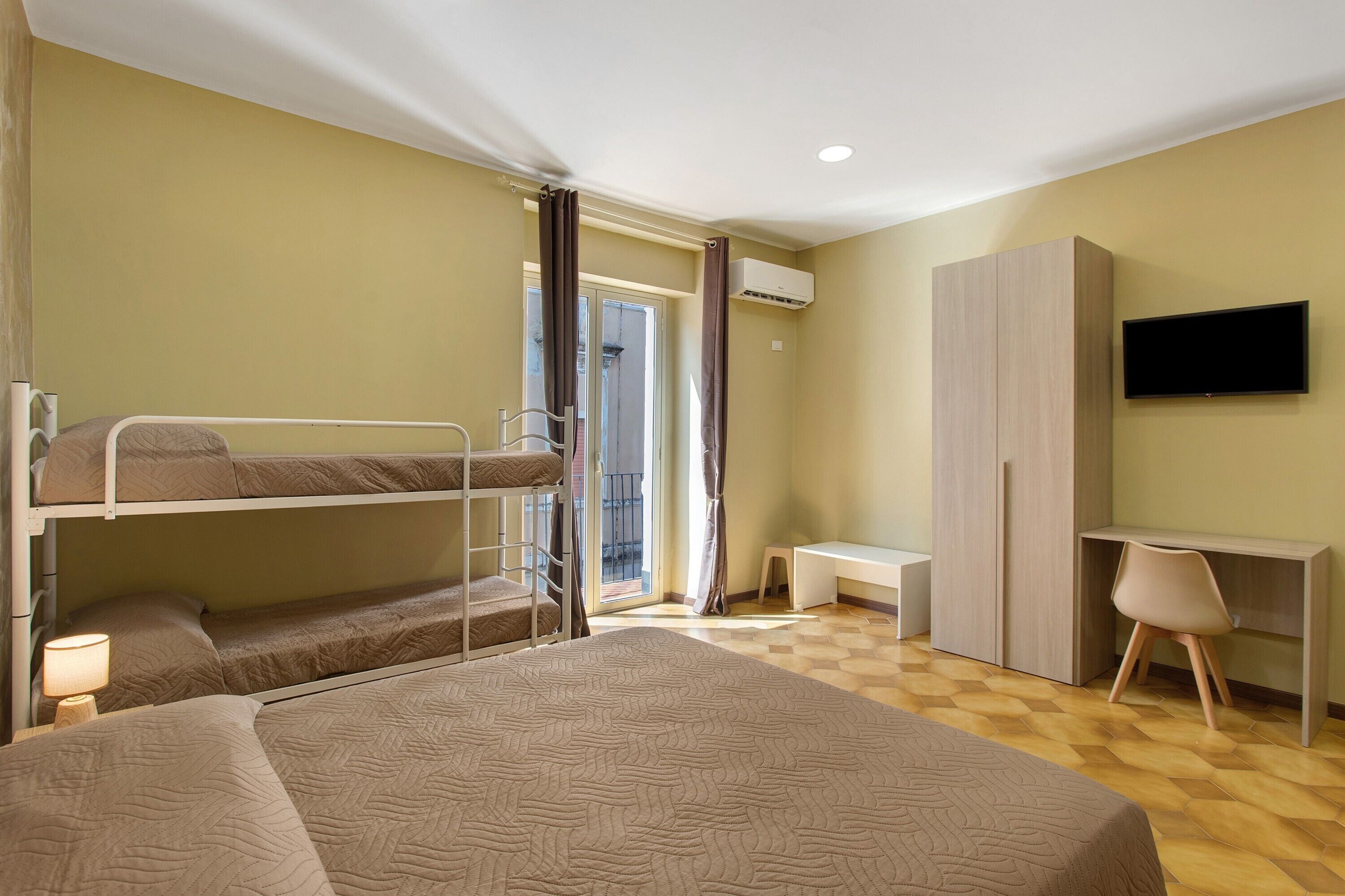 Een hotelkamer met stapelbedden, een bureau, een stoel, een televisie en een airconditioning.