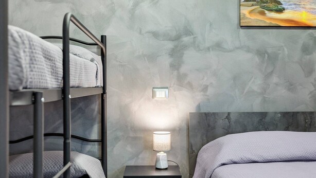 Un letto a castello con un comodino e una lampada, un quadro al muro e un letto con una coperta trapuntata.