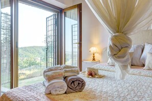 A bedroom with a large window, a bed with a canopy, a bedside table with a lamp, and a view of a green landscape. - SECLUDED BARN nestled in the vineyards. Private garden and breathtaking views. (Sinalunga)