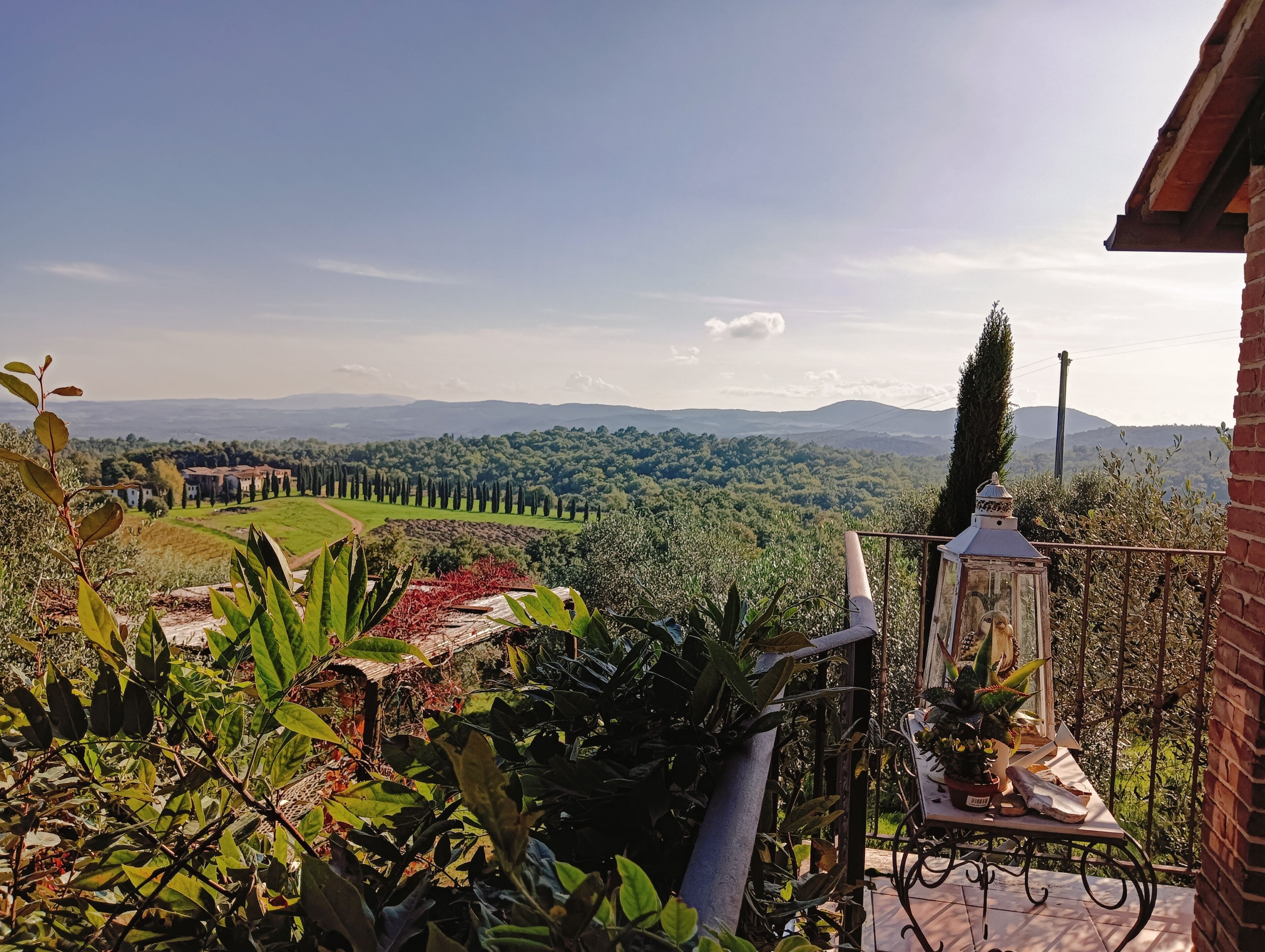 A terrace with a view of a countryside landscape, including a row of trees and distant hills.