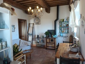 A cozy room with a wooden ceiling, a chandelier, a bed, a dining table, and various kitchen items.