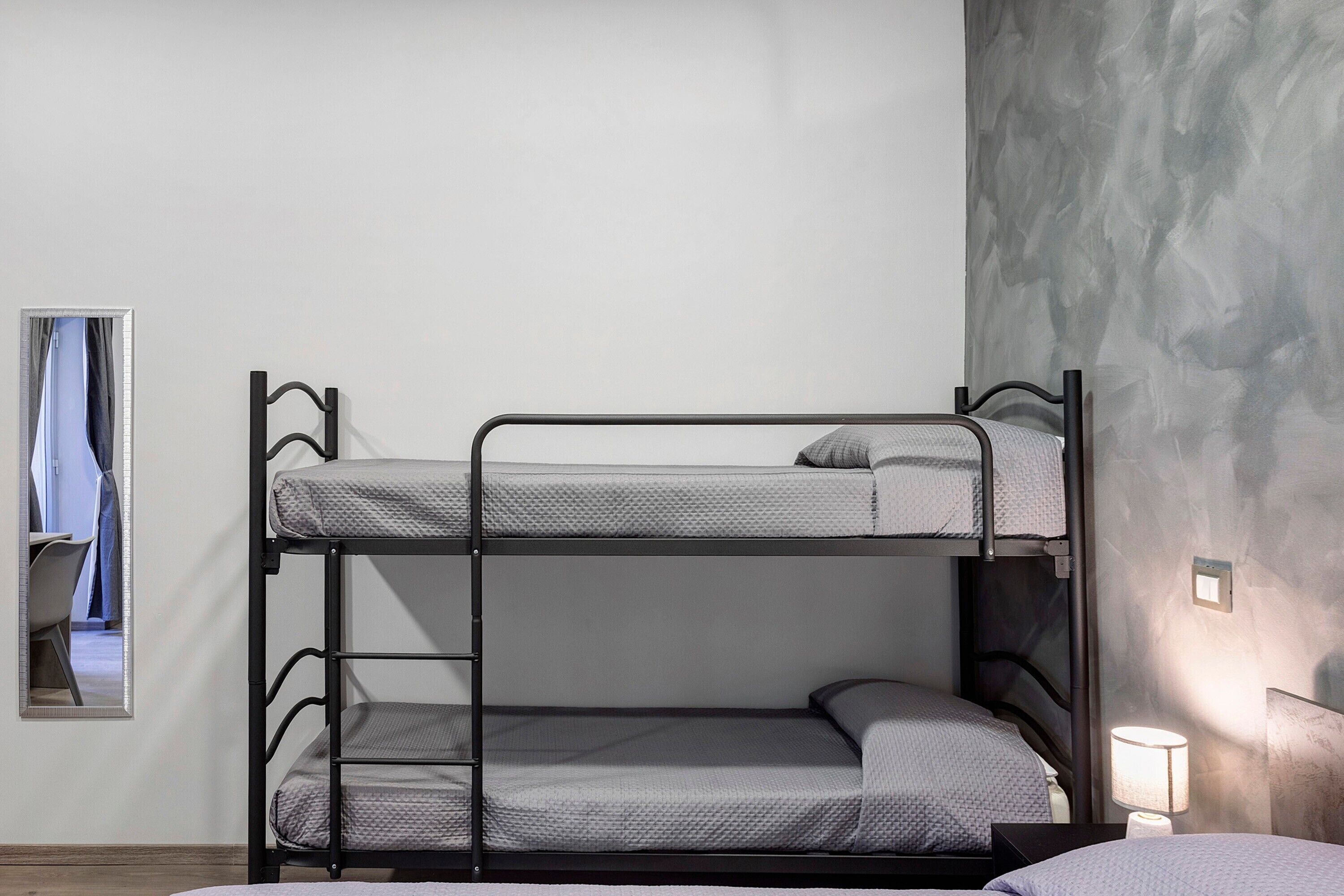 Een stapelbed met een ladder, een nachtkastje met een lamp en een spiegel aan de muur.