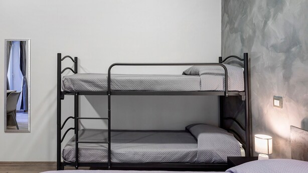 Una cama litera con escalera, una mesita de noche con lámpara y un espejo en la pared.
