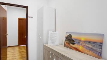 A hallway with a wooden floor, a white door, and a cabinet with a painting of a sunset over the ocean.