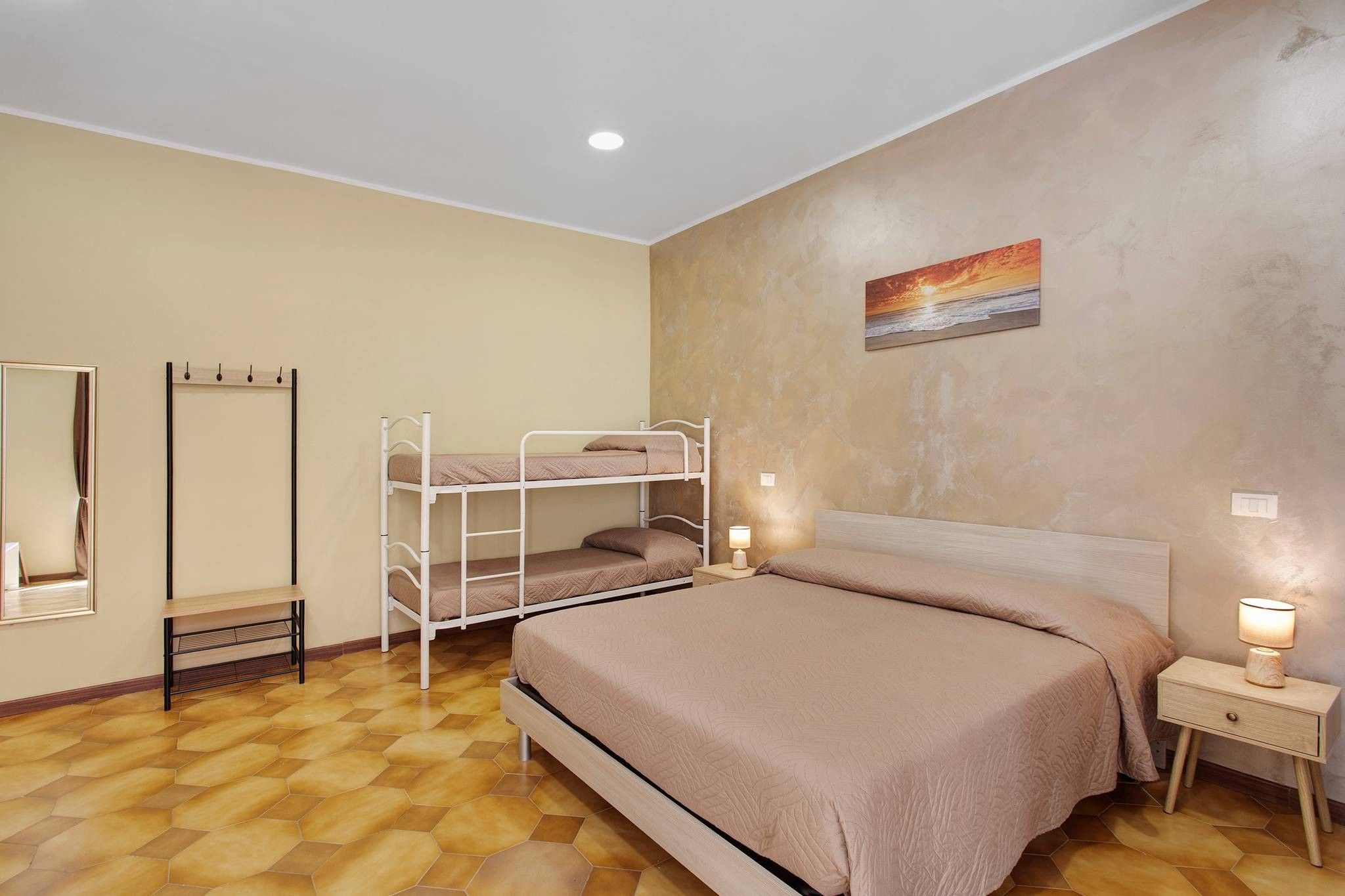 A bedroom with a bunk bed, a bedside table with a lamp, a mirror, and a painting on the wall.