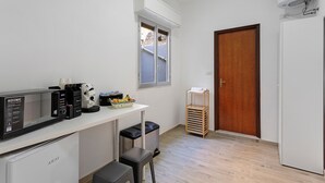 Cocina compacta equipada con microondas, cafetera y refrigerador pequeño. Hay una ventana sobre la encimera y una puerta a la derecha.