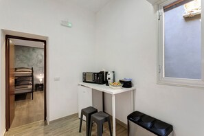 A compact kitchenette with a microwave, coffee maker, and a small refrigerator. There is a window with a view of the outside, and a door leading to a bathroom with a towel rack. - Dimora Sophia Nicole: In the Heart of Catania’s Charm (Catania)