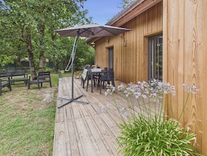 A wooden deck with outdoor seating, a table with chairs, and a large umbrella. - Pool, garden & kids’ games – House for 6 (Lanton)