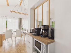 A modern kitchen with a built-in microwave, coffee maker, and toaster. There is a dining area with chairs and a table. - Pool, garden & kids’ games – House for 6 (Lanton)
