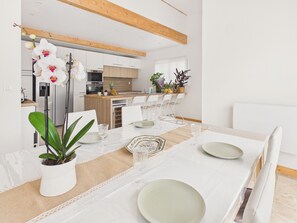 A modern dining area with a white table set for four, a kitchen in the background, and a potted plant on the table. - Pool, garden & kids’ games – House for 6 (Lanton)