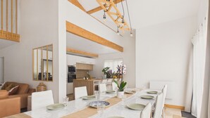 A spacious dining area with a long table set for a meal, a kitchen in the background, and a living area with a sofa and cushions. - Pool, garden & kids’ games – House for 6 (Lanton)