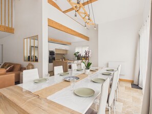 A spacious dining area with a long table set for a meal, a kitchen in the background, and a living area with a sofa and cushions. - Pool, garden & kids’ games – House for 6 (Lanton)