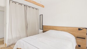 A bedroom with a wooden headboard, a bed with white bedding, and a curtain partially drawn. - Pool, garden & kids’ games – House for 6 (Lanton)
