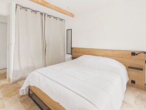 A bedroom with a wooden headboard, a bed with white bedding, and a curtain partially drawn. - Pool, garden & kids’ games – House for 6 (Lanton)