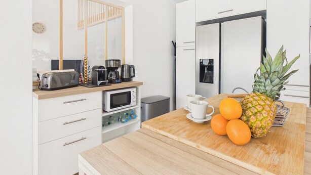 A modern kitchen with white cabinetry, a wooden countertop, a built-in oven, a coffee maker, and a fruit bowl with oranges and a pineapple. - Pool, garden & kids’ games – House for 6 (Lanton)