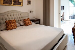 Ein Schlafzimmer mit einem großen Bett, zwei Zierkissen, einem kleinen Nachttisch, einem an der Wand montierten Fernseher und Blick ins Freie.