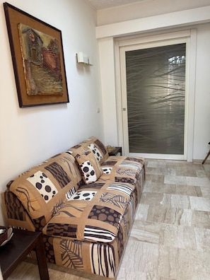 A living room with a patterned sofa, a painting on the wall, and a sliding glass door. - Apartment in a Villa with a Garden (Roma)