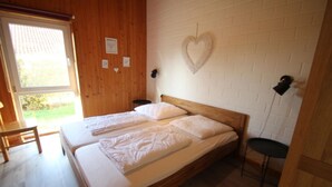A room with a wooden floor, a bed with white bedding, a small table, and a heart-shaped decoration on the wall. - Moderner Bungalow mit Terrasse im Ferienpark Mirow (Granzow)