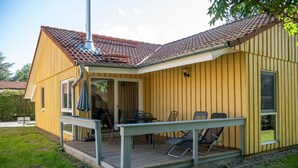 Keltainen rakennus, jossa on katettu terassi, savupiippu ja terassilla olevia tuoleja.