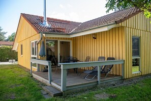 Ein gelbes Gebäude mit einer überdachten Terrasse, einem Schornstein und einer Deck mit Stühlen.