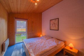 Una habitación con paneles de madera, una cama, una ventana, un cuadro colgado en la pared y una mesita de noche con una lámpara.