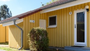 A yellow building with a white door and window, number 16, and a small bush in front. - Komfortabler Doppelbungalow mit Terrasse im Ferienpark Mirow (Granzow)