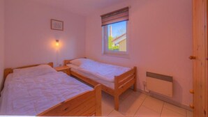 A bedroom with two wooden beds, a window with a view, a radiator, and a door. - Komfortabler Doppelbungalow mit Terrasse im Ferienpark Mirow (Granzow)