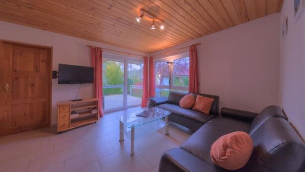 A living room with a glass coffee table, a sofa, a television, and a sliding glass door leading to an outdoor area. - Heimeliger Doppelbungalow mit Terrasse im Ferienpark Mirow (Granzow)