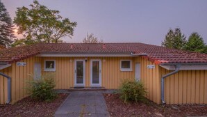 A two-story building with a red-tiled roof, a central entrance with a door, and two windows on the upper floor. - Heimeliger Doppelbungalow mit Terrasse im Ferienpark Mirow (Granzow)