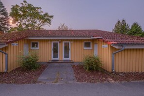 A two-story building with a red-tiled roof, a central entrance with a door, and two windows on the upper floor. - Heimeliger Doppelbungalow mit Terrasse im Ferienpark Mirow (Granzow)