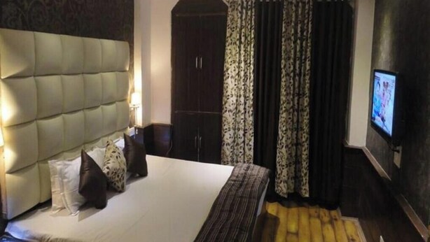 A hotel room with a large bed, a wardrobe, a television, and a patterned curtain. - Hotel Sunrise (Shimla)