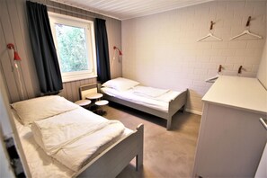 Ein Zimmer mit zwei Betten, einem kleinen Tisch, einem Fenster mit Vorhängen, einem Heizkörper und einem weißen Schrank.