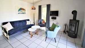 Ein Wohnzimmer mit einem dunkelblauen Sofa, einem hellblauen Sessel, einem kleinen runden Tisch, einem Fernseher und einem Kaminofen.