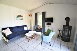 Ein Wohnzimmer mit einem dunkelblauen Sofa, einem hellblauen Sessel, einem kleinen runden Tisch, einem Fernseher und einem Kaminofen.
