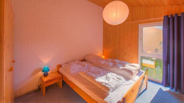 Et soveværelse med en enkelt seng, et natbord med lampe, træloft og et vindue med gardiner.
