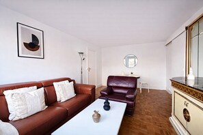 A living room with a brown leather sofa, a white coffee table, a purple leather armchair, a small side table, and a decorative mirror. - Appartement charmant près du parc Montsouris (Paris)
