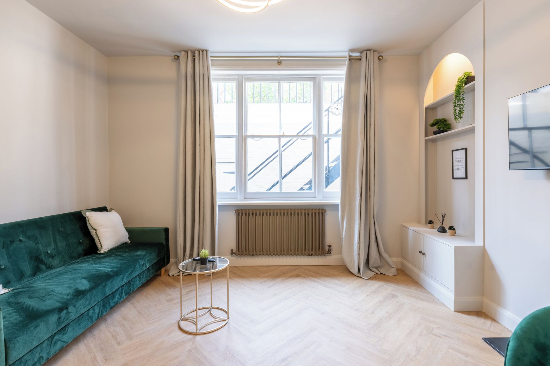 Una sala de estar moderna con un sofá verde, una mesa redonda de vidrio, un radiador y una ventana con cortinas.