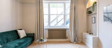 Una sala de estar moderna con un sofá verde, una mesa redonda de vidrio, un radiador y una ventana con cortinas.
