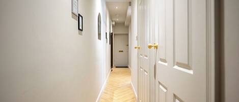 A hallway with white walls, wooden flooring, and doors with golden handles.
