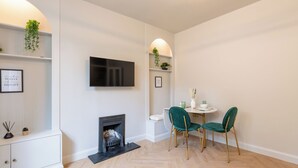 Un salon moderne avec une cheminée, un téléviseur fixé au mur et un coin repas avec deux chaises.