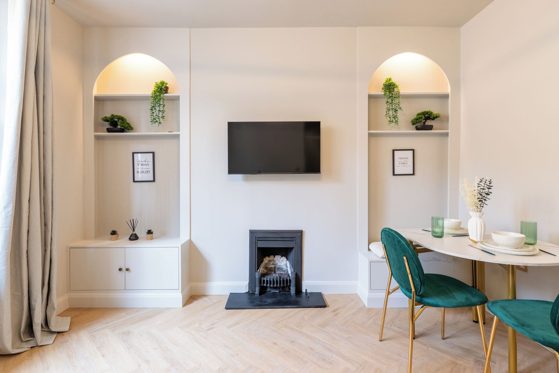 Een moderne woonkamer met een open haard, een flatscreen televisie en een eethoek met groene stoelen.