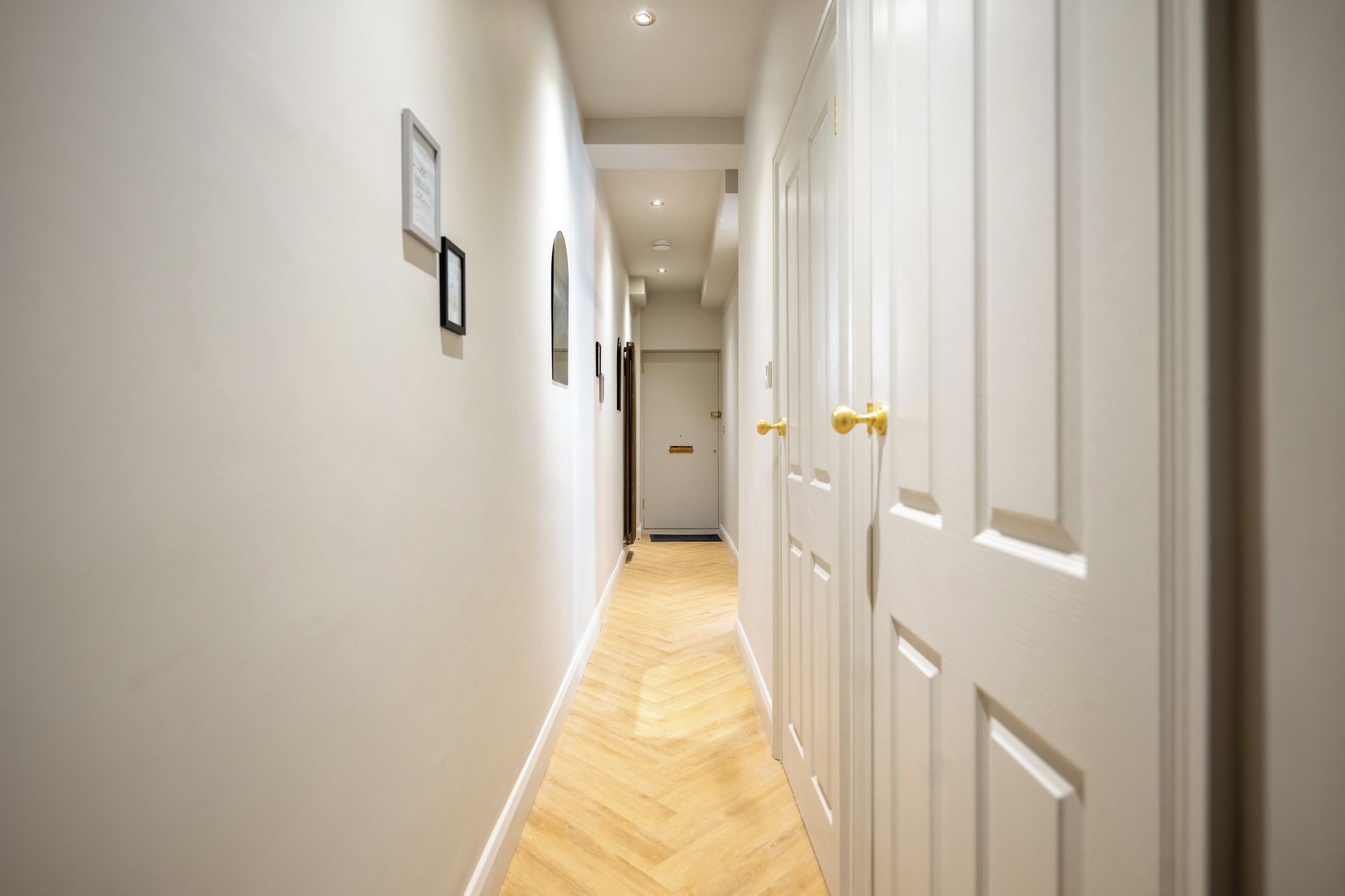 Un couloir aux murs blancs, au plancher en bois et aux portes dotées de poignées dorées.