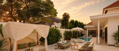 Une terrasse extérieure paisible, dotée d’un lit à baldaquin, de chaises longues, d’une piscine et d’une végétation luxuriante.