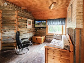 A log cabin interior with a wooden ceiling, a television mounted on the wall, a wooden sofa, a rocking chair, and a small wooden chest. - Ylläs 1 by Interhome (Ylläsjärvi)