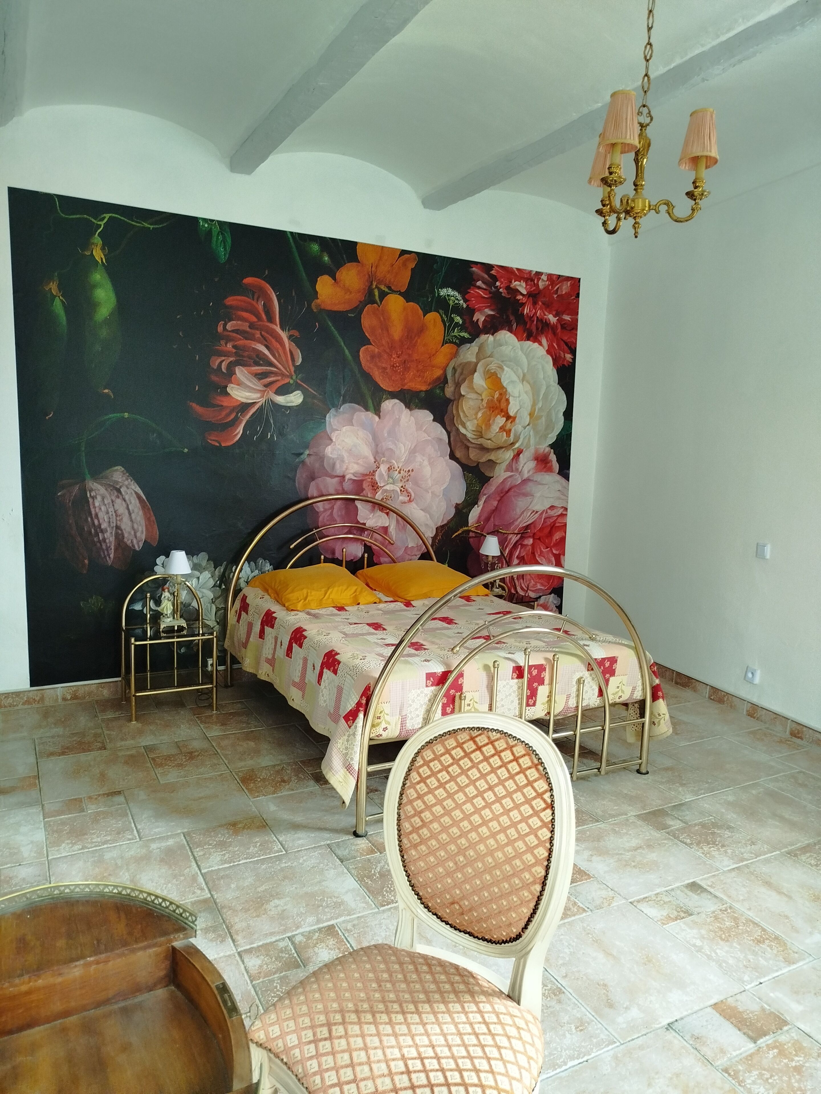 Een slaapkamer met een bed, een stoel, een schilderij aan de muur en een kroonluchter.