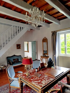 Une pièce avec un lustre, un escalier, un canapé bleu, une table rouge et un miroir.