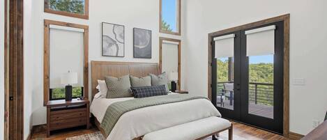 A bedroom with a bed, nightstands, a bench, a ceiling fan, and large windows.