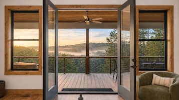 A room with a wooden deck, a chair, and a view of a forested landscape.