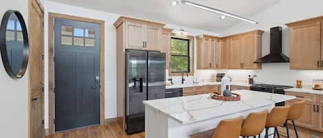 Una cocina moderna con armarios de madera, un refrigerador negro, una isla de mármol y taburetes de bar.