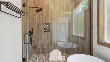 A modern bathroom with a glass shower enclosure, a white bathtub, and a stone-tiled shower floor.
